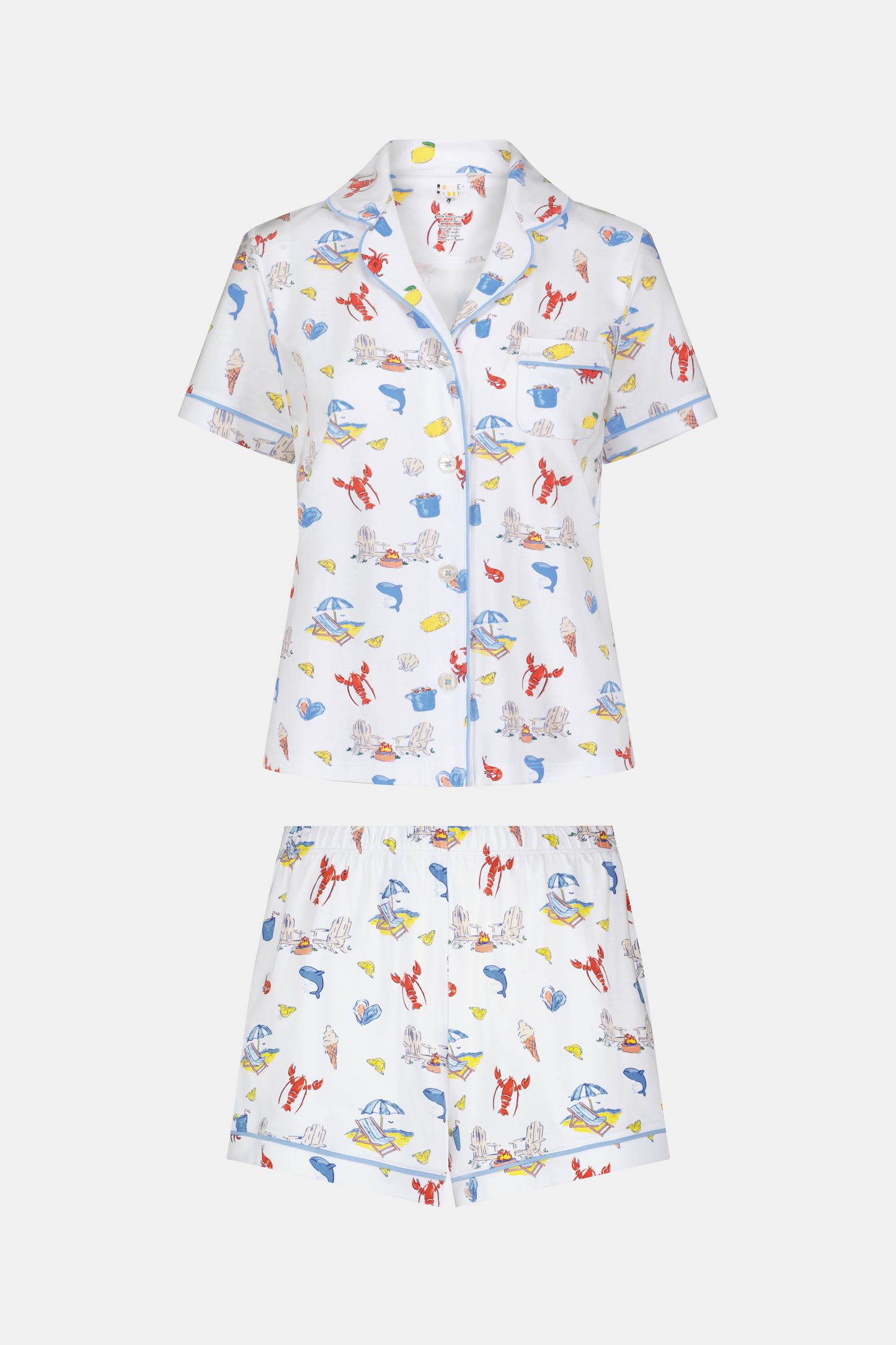 A woman stands barefoot in Roller Rabbit's Catch of the Day Polo Pajamas—short-sleeve, button-up PJs with matching shorts, both featuring a colorful seaside print—facing forward against a plain white background.