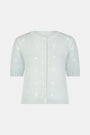 Close-up of a woman wearing the Roller Rabbit Floral Bloom Nyla Cardigan, a light blue cotton button-up with white embroidered stars, rounded neckline, and short sleeves, styled with white eyelet shorts.