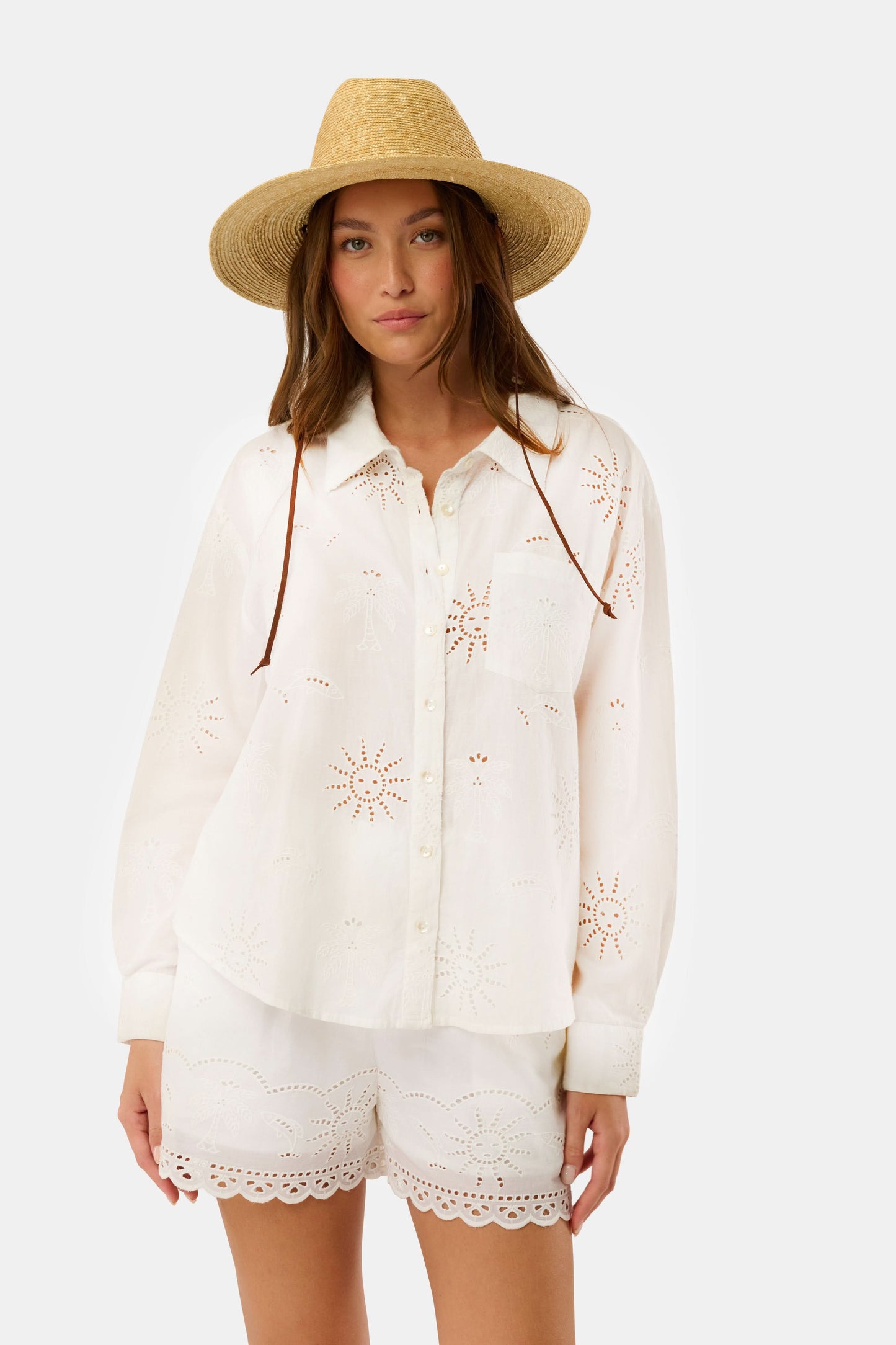 A woman in a straw hat and white scalloped shorts wears the Roller Rabbit Sunny Days Eyelet Girlfriend Shirt, standing against a plain light background.