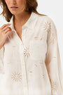 A woman in a straw hat and white scalloped shorts wears the Roller Rabbit Sunny Days Eyelet Girlfriend Shirt, standing against a plain light background.