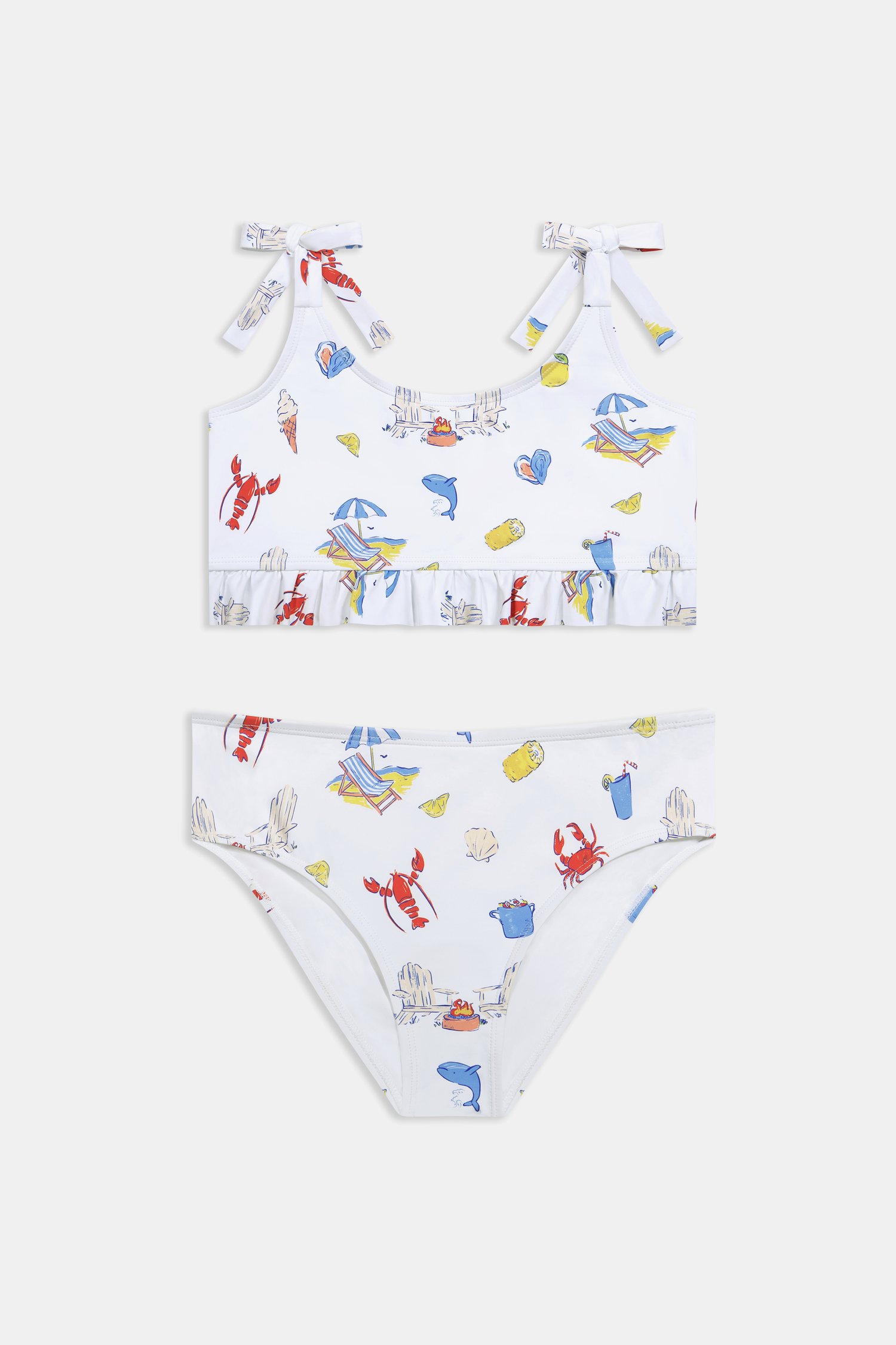 A girl wears the Roller Rabbit Kids Ruffle Catch of the Day Cora Bikini, a white two-piece with a playful print, ruffle trim top, and tie straps, standing against a plain light background.
