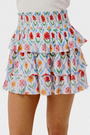 A close-up of the Roller Rabbit Infinity Floral Siggy Skirt, a crinkle chiffon mini with ruffles, featuring red, yellow, pink, and green florals on white. The skirt is styled with a white top.