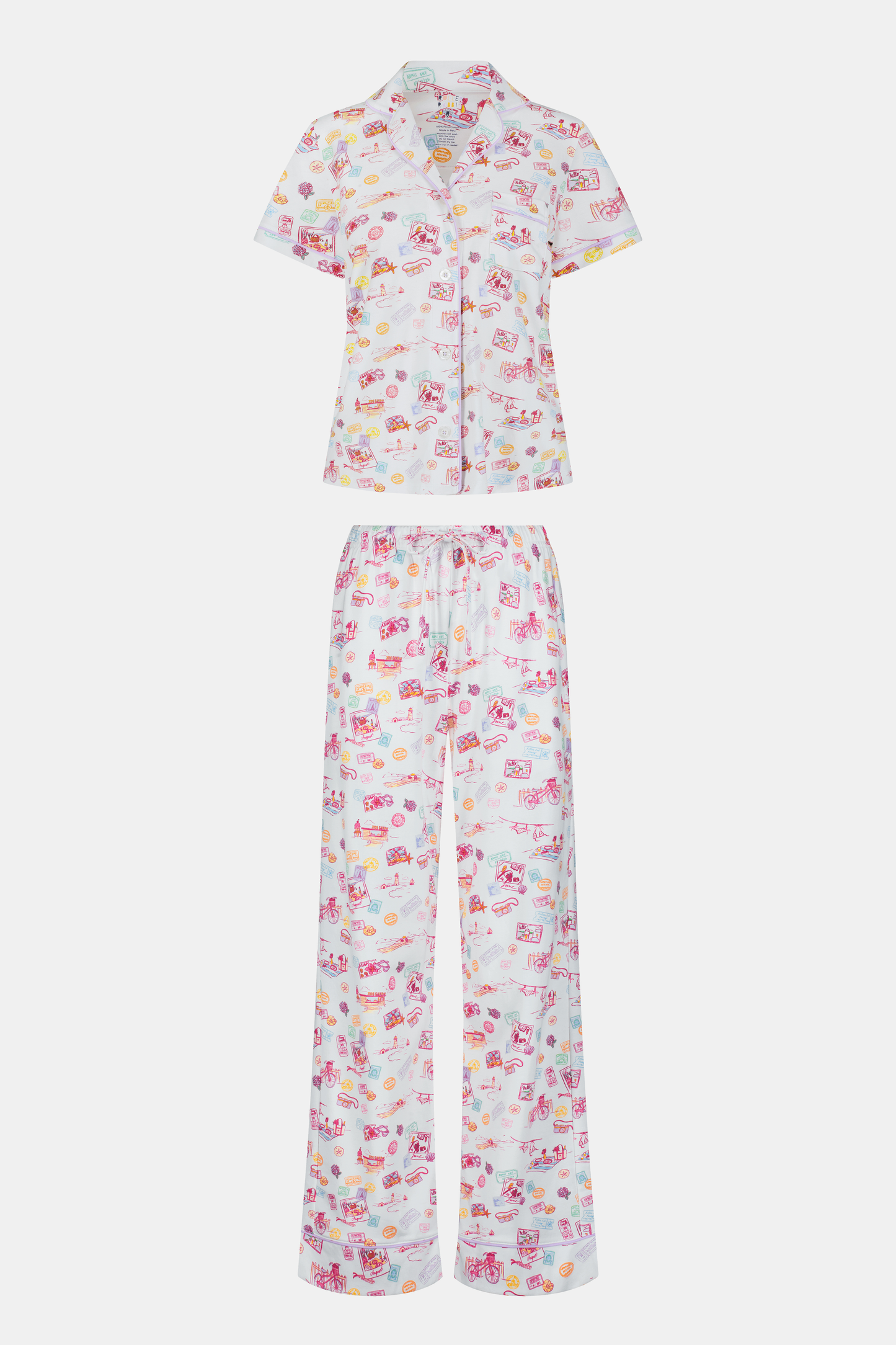 A woman with curly hair models the Roller Rabbit Summer Memories Fiora Pajamas, a Pima cotton set with a colorful sushi print, including a short-sleeve button-up top and long pants, against a white background.