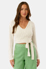 A woman wearing the Roller Rabbit Pointelle Cassidy Sweater paired with green high-waisted pants featuring white embroidered details, standing against a plain light background.