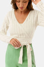 A woman wearing the Roller Rabbit Pointelle Cassidy Sweater paired with green high-waisted pants featuring white embroidered details, standing against a plain light background.