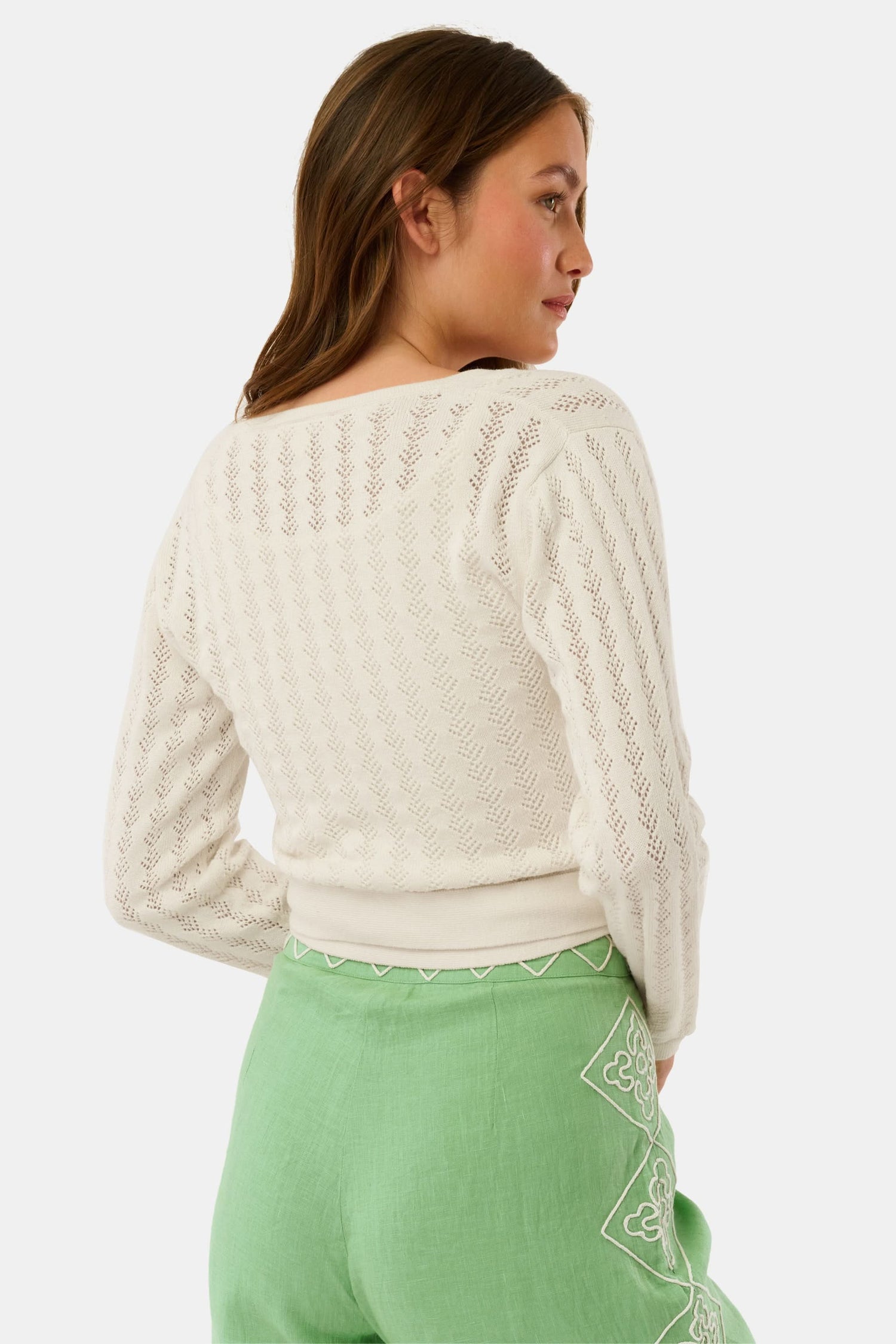 A woman wearing the Roller Rabbit Pointelle Cassidy Sweater paired with green high-waisted pants featuring white embroidered details, standing against a plain light background.