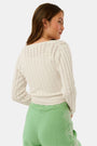 A woman wearing the Roller Rabbit Pointelle Cassidy Sweater paired with green high-waisted pants featuring white embroidered details, standing against a plain light background.