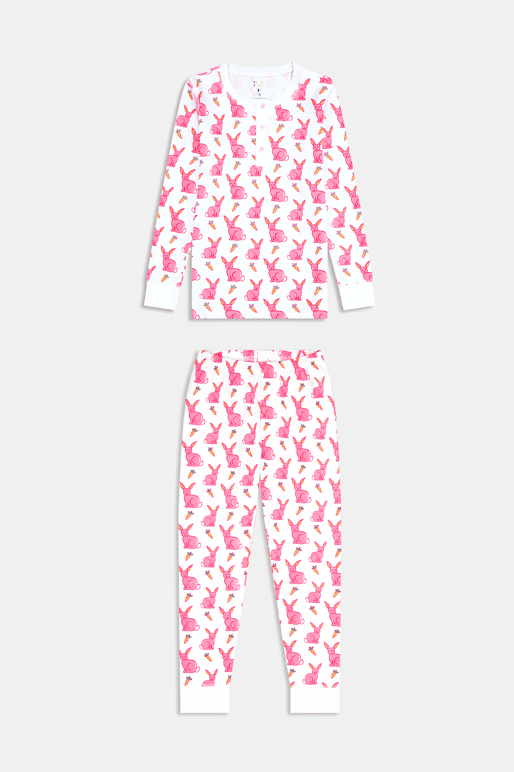 A young girl smiles barefoot in Roller Rabbit’s Kids Romy the Rabbit Pajamas, a soft Pima cotton long-sleeve set with a playful rabbit print; her brown hair frames her face against a simple, light background.