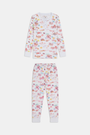 A young girl smiles barefoot in Roller Rabbit Kids Summer Memories Pajamas, made from soft Pima Cotton with playful, colorful prints on white. She stands against a light gray background. Made in Peru.