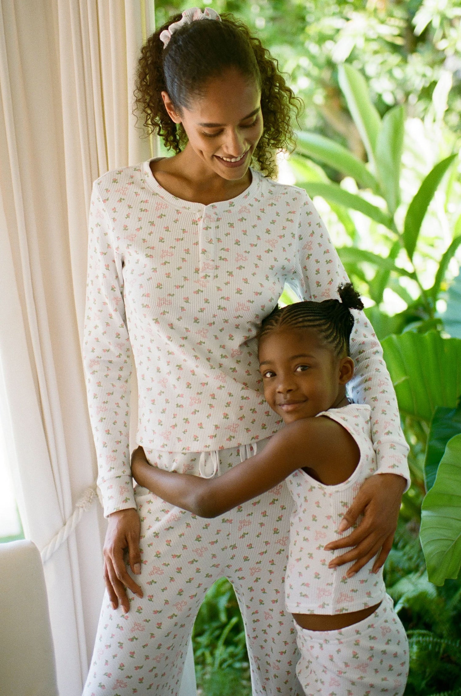 A woman wears the Mini Monkey Blossom Rosemary Top by Roller Rabbit, featuring a white pima cotton fabric with a small pink floral pattern, standing facing forward against a light background with her hands at her sides.