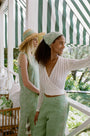 A woman wearing the Roller Rabbit Pointelle Cassidy Sweater paired with green high-waisted pants featuring white embroidered details, standing against a plain light background.