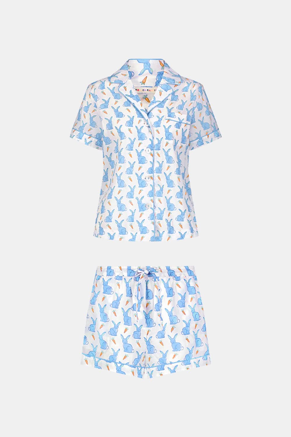 A woman wears the Roller Rabbit Romy the Rabbit Livy Set, a light blue cotton two-piece loungewear featuring a colorful bunny print, as she stands smiling against a plain white background.