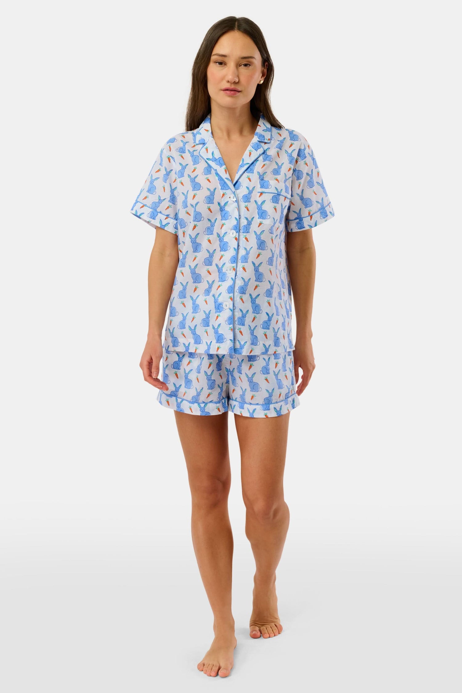 A woman wears the Roller Rabbit Romy the Rabbit Livy Set, a light blue cotton two-piece loungewear featuring a colorful bunny print, as she stands smiling against a plain white background.