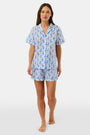 A woman wears the Roller Rabbit Romy the Rabbit Livy Set, a light blue cotton two-piece loungewear featuring a colorful bunny print, as she stands smiling against a plain white background.