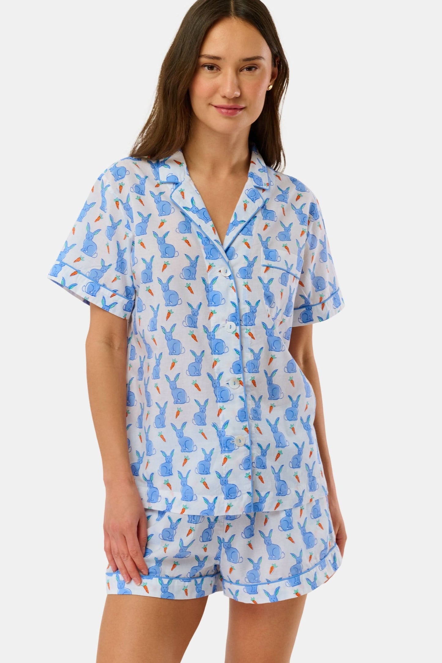 A woman wears the Roller Rabbit Romy the Rabbit Livy Set, a light blue cotton two-piece loungewear featuring a colorful bunny print, as she stands smiling against a plain white background.