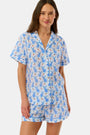 A woman wears the Roller Rabbit Romy the Rabbit Livy Set, a light blue cotton two-piece loungewear featuring a colorful bunny print, as she stands smiling against a plain white background.
