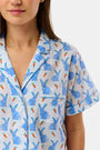 A woman wears the Roller Rabbit Romy the Rabbit Livy Set, a light blue cotton two-piece loungewear featuring a colorful bunny print, as she stands smiling against a plain white background.