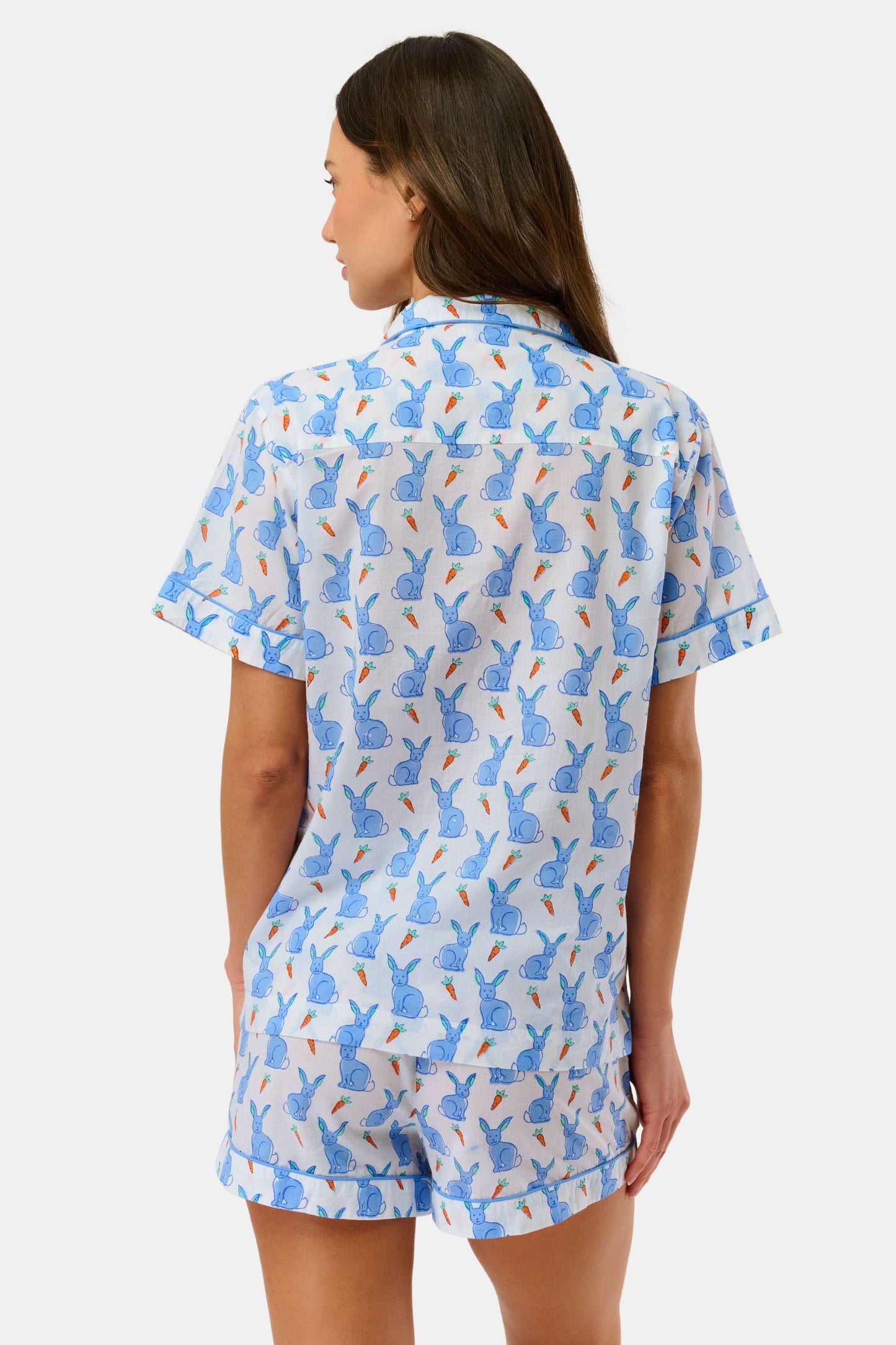 A woman wears the Roller Rabbit Romy the Rabbit Livy Set, a light blue cotton two-piece loungewear featuring a colorful bunny print, as she stands smiling against a plain white background.
