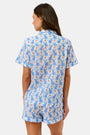 A woman wears the Roller Rabbit Romy the Rabbit Livy Set, a light blue cotton two-piece loungewear featuring a colorful bunny print, as she stands smiling against a plain white background.
