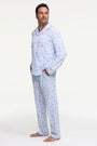 A man stands barefoot on a white background wearing Roller Rabbit's Mens Starry Nights Lattice Long Sleeve Polo Pajamas, featuring light blue and white patterns. He smiles with one hand in his pocket, highlighting the comfort of these matching PJs.