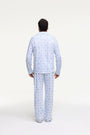 A man stands barefoot on a white background wearing Roller Rabbit's Mens Starry Nights Lattice Long Sleeve Polo Pajamas, featuring light blue and white patterns. He smiles with one hand in his pocket, highlighting the comfort of these matching PJs.
