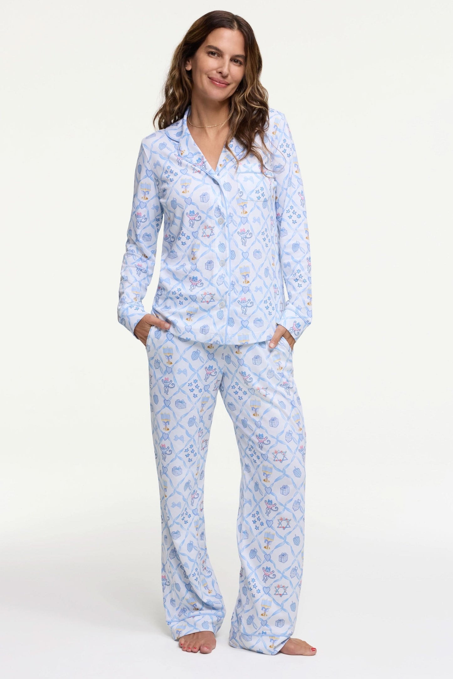 A woman smiles barefoot on a white background, hands in pockets, wearing Roller Rabbit's Starry Nights Lattice Long Sleeve Polo Pajamas—cozy loungewear crafted from soft Pima cotton.