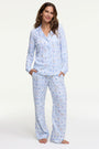 A woman smiles barefoot on a white background, hands in pockets, wearing Roller Rabbit's Starry Nights Lattice Long Sleeve Polo Pajamas—cozy loungewear crafted from soft Pima cotton.