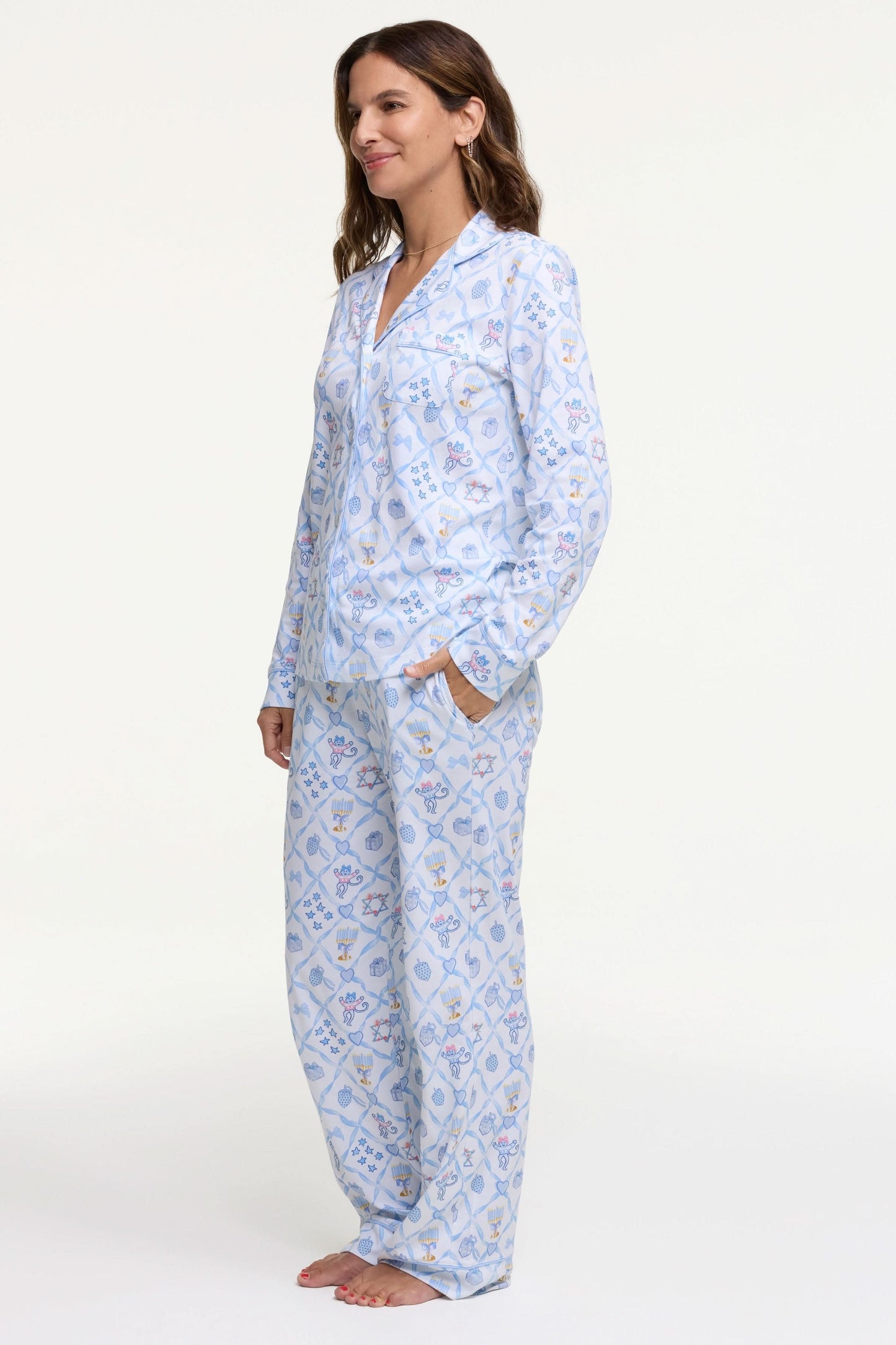 A woman smiles barefoot on a white background, hands in pockets, wearing Roller Rabbit's Starry Nights Lattice Long Sleeve Polo Pajamas—cozy loungewear crafted from soft Pima cotton.