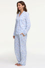 A woman smiles barefoot on a white background, hands in pockets, wearing Roller Rabbit's Starry Nights Lattice Long Sleeve Polo Pajamas—cozy loungewear crafted from soft Pima cotton.