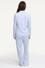 A woman smiles barefoot on a white background, hands in pockets, wearing Roller Rabbit's Starry Nights Lattice Long Sleeve Polo Pajamas—cozy loungewear crafted from soft Pima cotton.