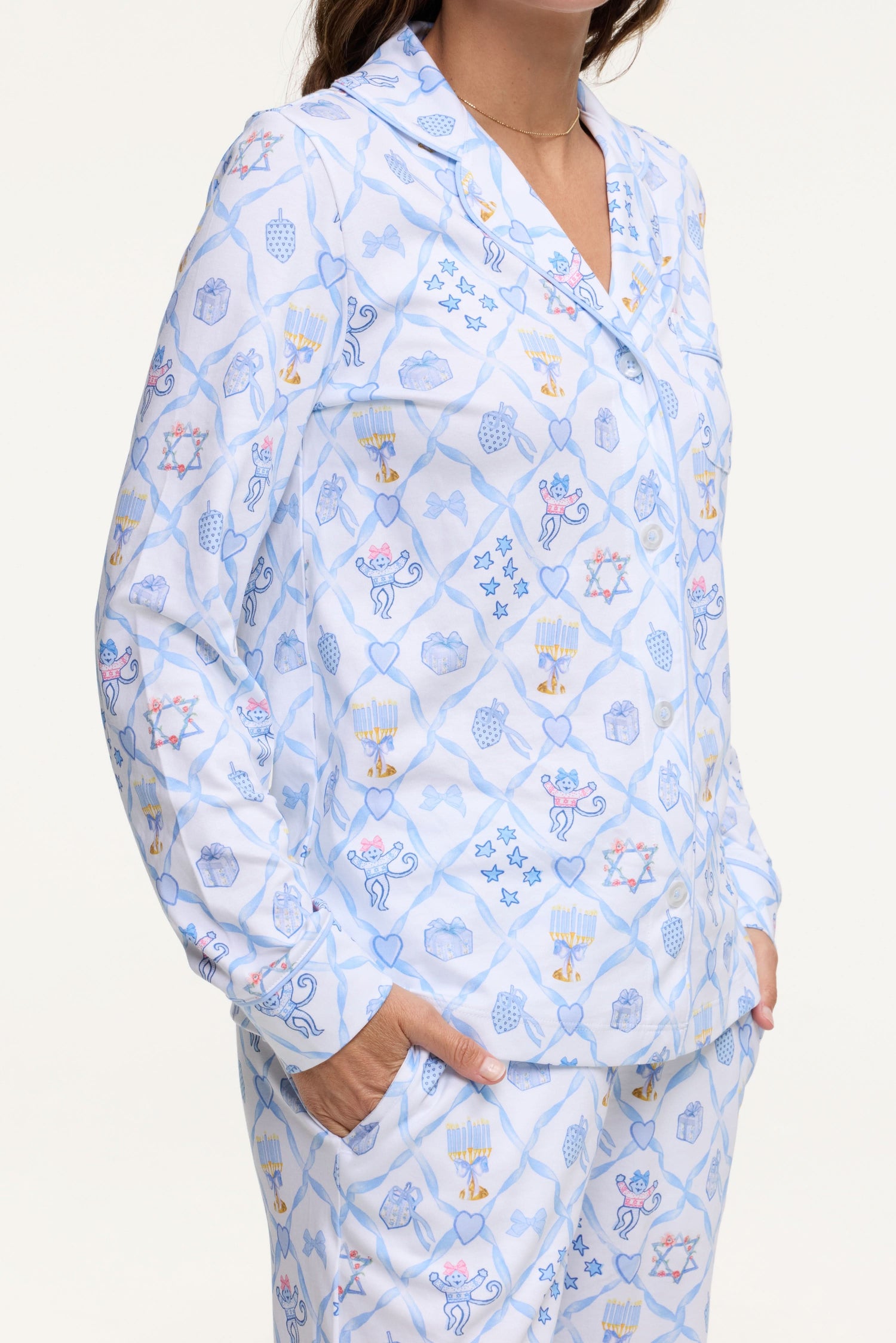 A woman smiles barefoot on a white background, hands in pockets, wearing Roller Rabbit's Starry Nights Lattice Long Sleeve Polo Pajamas—cozy loungewear crafted from soft Pima cotton.
