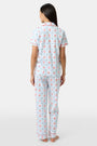 A woman in Roller Rabbit’s 4th of Jemina Fiora Pajamas and pink slippers relaxes on the bow of a blue boat at a marina while another person in white sleepwear stands nearby, partially out of frame.