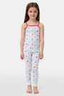A young girl stands barefoot, smiling against a light background. She wears the Roller Rabbit Kids 4th of Jemina Noa Set—matching white Pima Cotton pajamas with red trim and a colorful flowers, butterflies, and birds print.