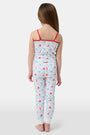 A young girl stands barefoot, smiling against a light background. She wears the Roller Rabbit Kids 4th of Jemina Noa Set—matching white Pima Cotton pajamas with red trim and a colorful flowers, butterflies, and birds print.