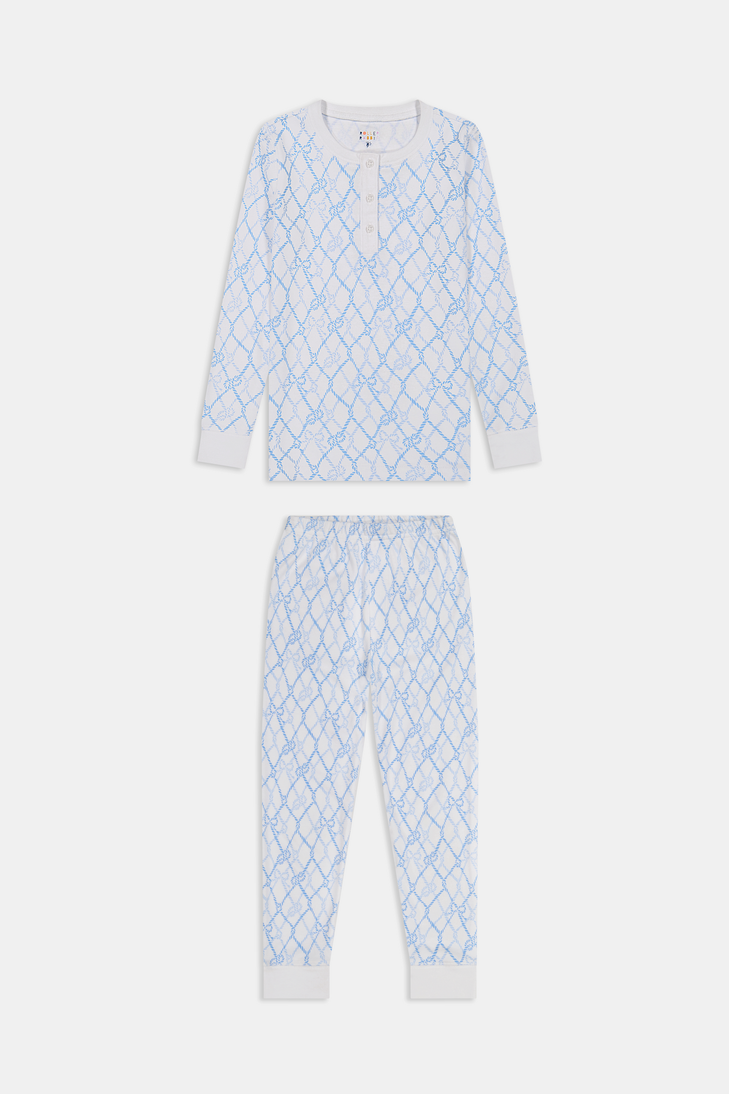 A young girl with long brown hair stands barefoot in Roller Rabbit Kids Seaside Knots Juniper Pajamas, featuring matching white and light blue knot print on soft Pima fabric with long sleeves and button details, against a plain light background.