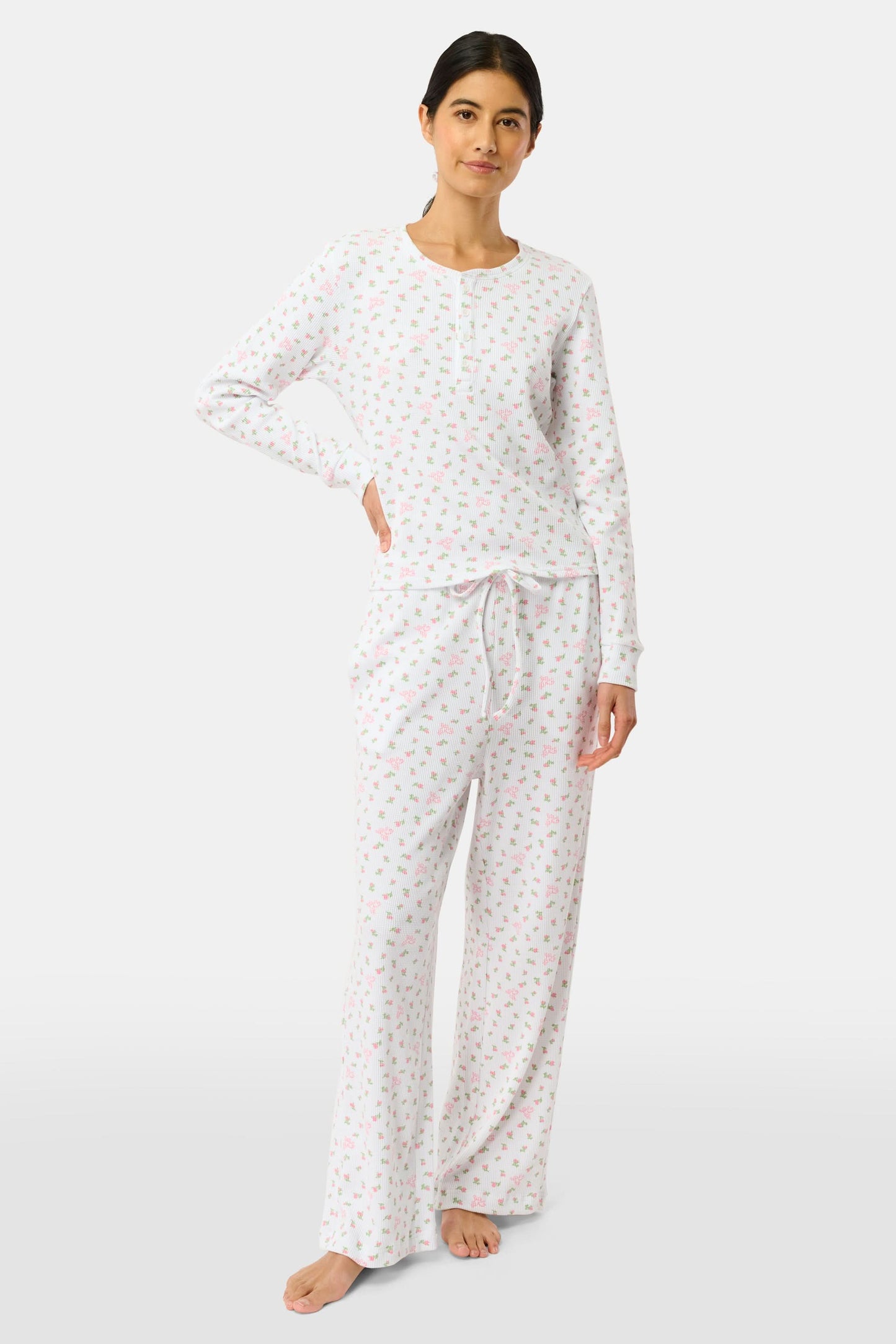 A woman wears the Mini Monkey Blossom Rosemary Top by Roller Rabbit, featuring a white pima cotton fabric with a small pink floral pattern, standing facing forward against a light background with her hands at her sides.
