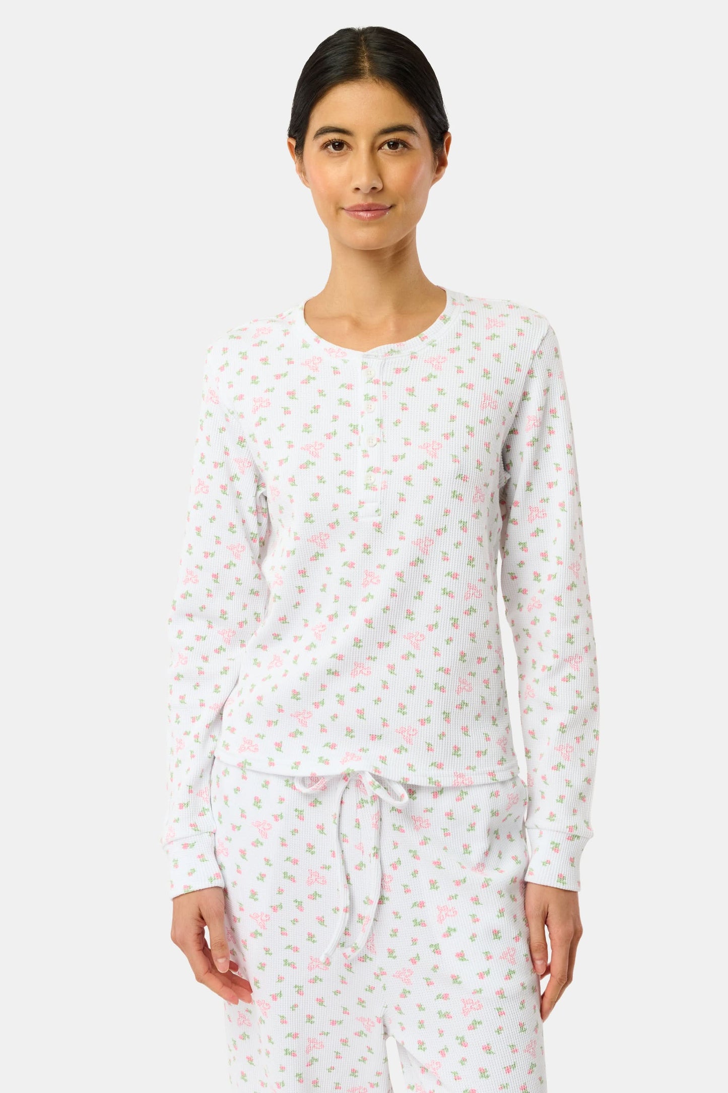 A woman wears the Mini Monkey Blossom Rosemary Top by Roller Rabbit, featuring a white pima cotton fabric with a small pink floral pattern, standing facing forward against a light background with her hands at her sides.