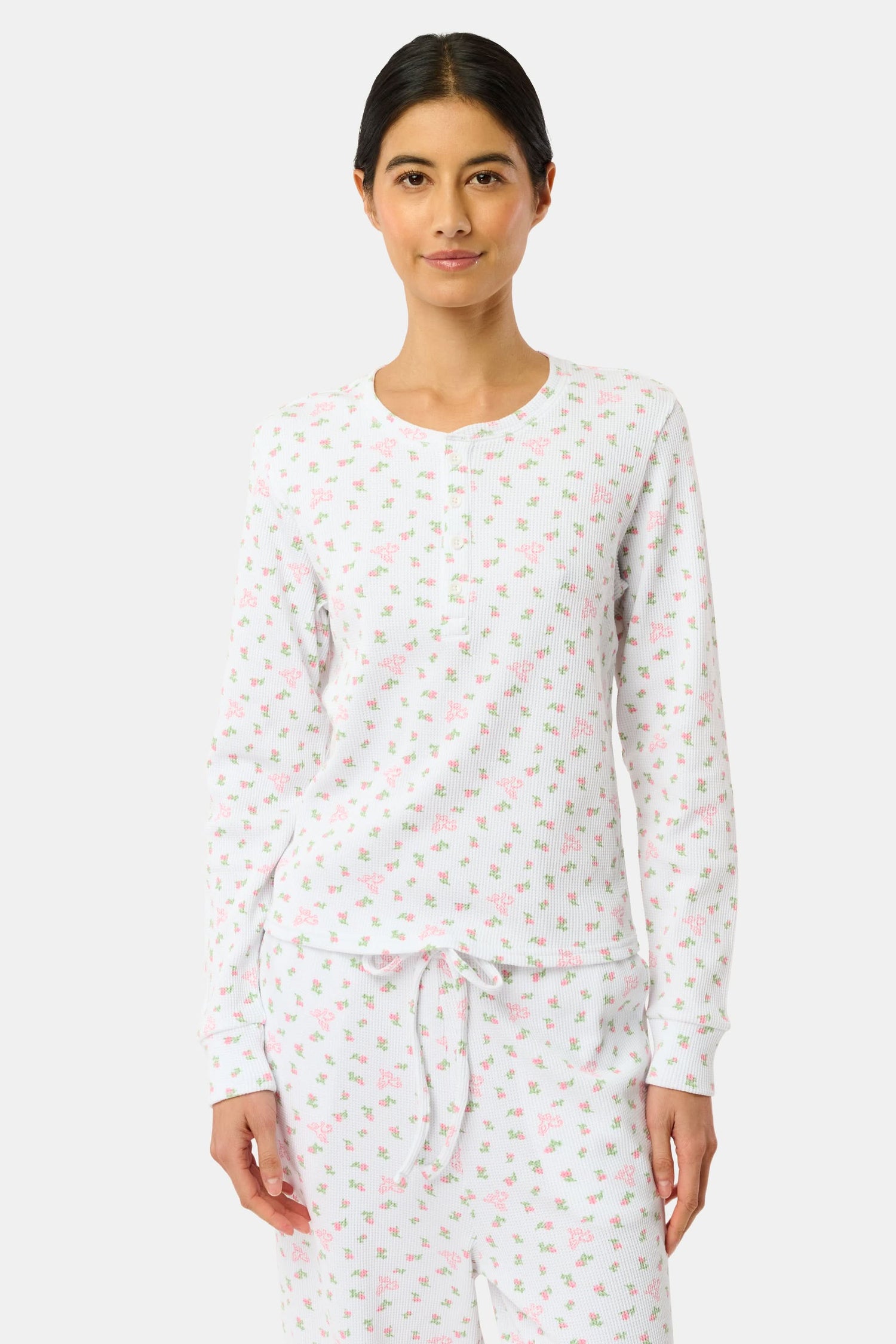 A woman wears the Mini Monkey Blossom Rosemary Top by Roller Rabbit, featuring a white pima cotton fabric with a small pink floral pattern, standing facing forward against a light background with her hands at her sides.
