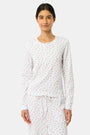 A woman wears the Mini Monkey Blossom Rosemary Top by Roller Rabbit, featuring a white pima cotton fabric with a small pink floral pattern, standing facing forward against a light background with her hands at her sides.