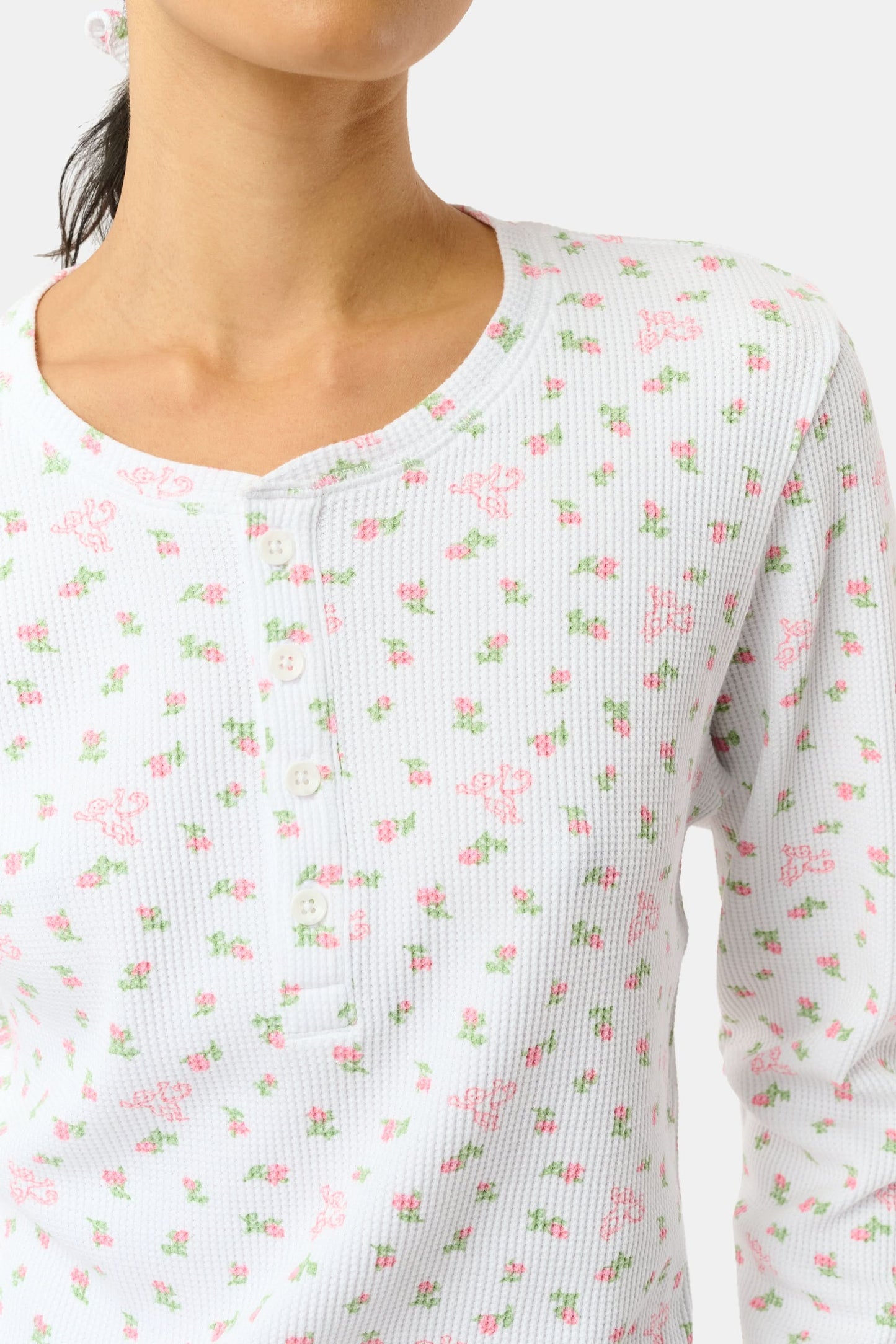 A woman wears the Mini Monkey Blossom Rosemary Top by Roller Rabbit, featuring a white pima cotton fabric with a small pink floral pattern, standing facing forward against a light background with her hands at her sides.