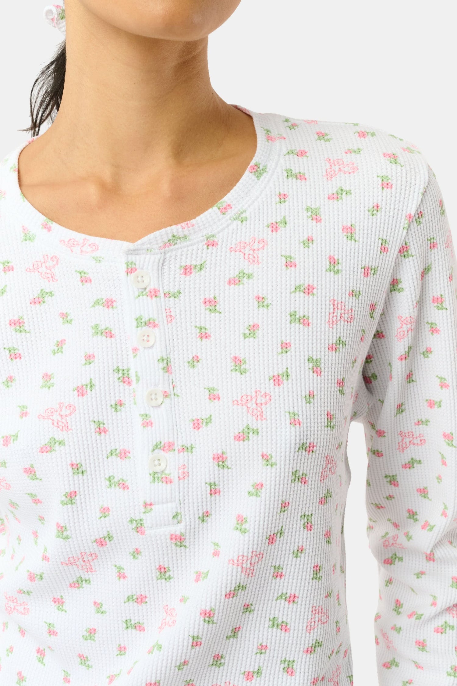A woman wears the Mini Monkey Blossom Rosemary Top by Roller Rabbit, featuring a white pima cotton fabric with a small pink floral pattern, standing facing forward against a light background with her hands at her sides.