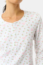 A woman wears the Mini Monkey Blossom Rosemary Top by Roller Rabbit, featuring a white pima cotton fabric with a small pink floral pattern, standing facing forward against a light background with her hands at her sides.