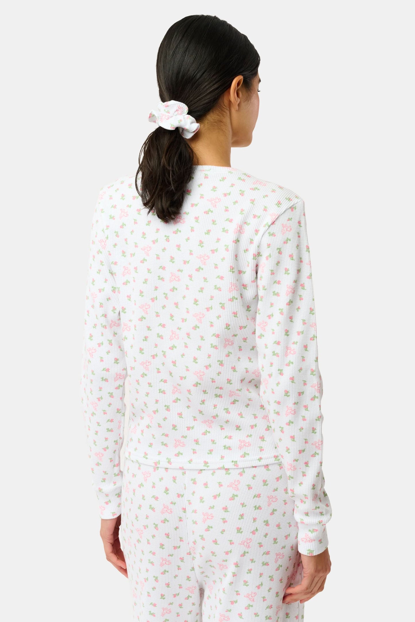 A woman wears the Mini Monkey Blossom Rosemary Top by Roller Rabbit, featuring a white pima cotton fabric with a small pink floral pattern, standing facing forward against a light background with her hands at her sides.