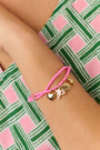 The Roller Rabbit Icon Party Charm Bracelet is a pink adjustable bracelet with five gold-tone charms—a heart, unicorn, butterfly, cat, and star—shown on a plain white background.