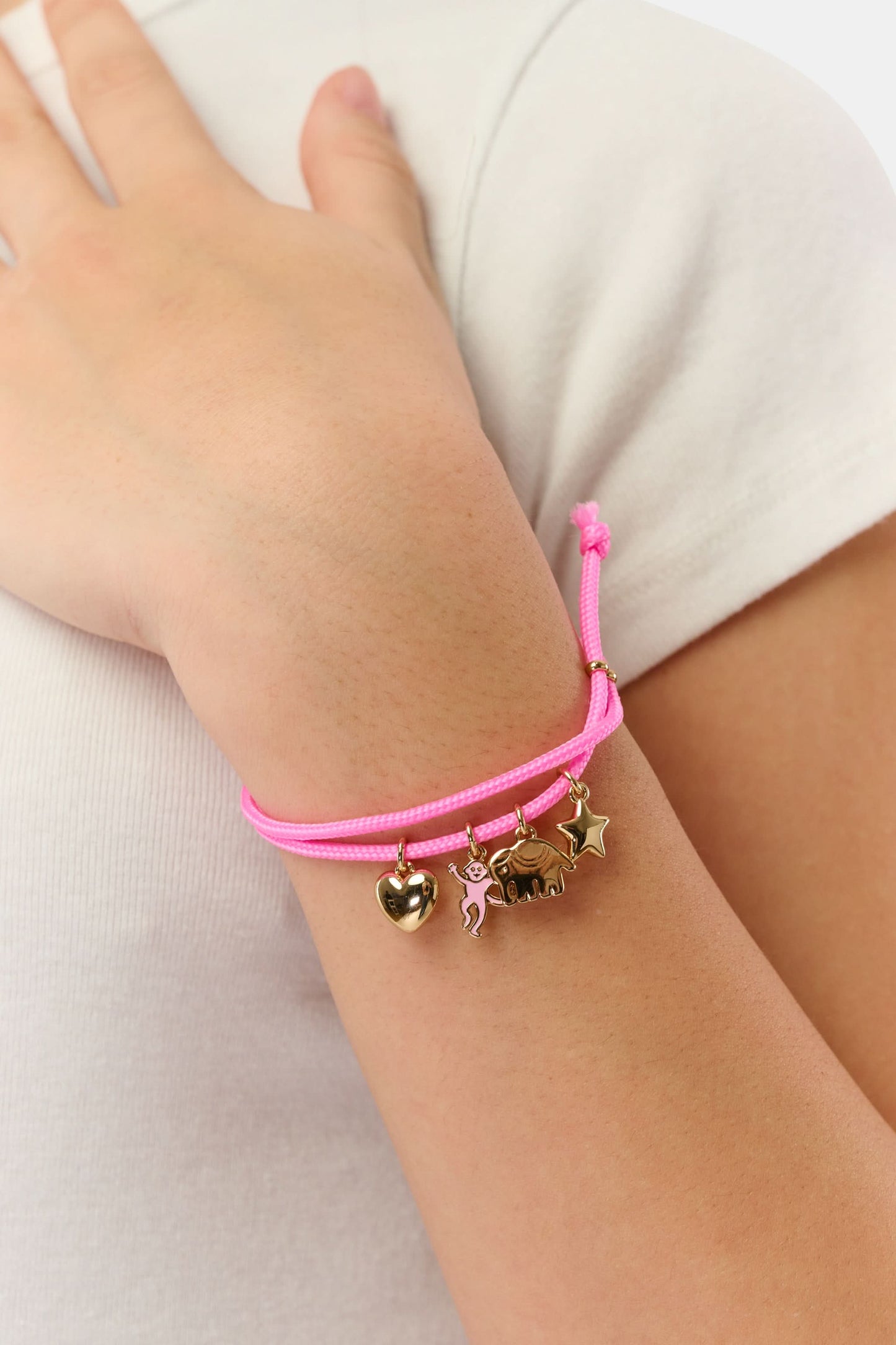 The Roller Rabbit Icon Party Charm Bracelet is a pink adjustable bracelet with five gold-tone charms—a heart, unicorn, butterfly, cat, and star—shown on a plain white background.
