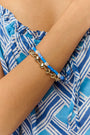 A person wearing a blue and white patterned off-shoulder top and the Roller Rabbit Colorful Hearts Bracelet Stack, featuring playful heart-shaped links and vibrant beads, on their crossed arm.