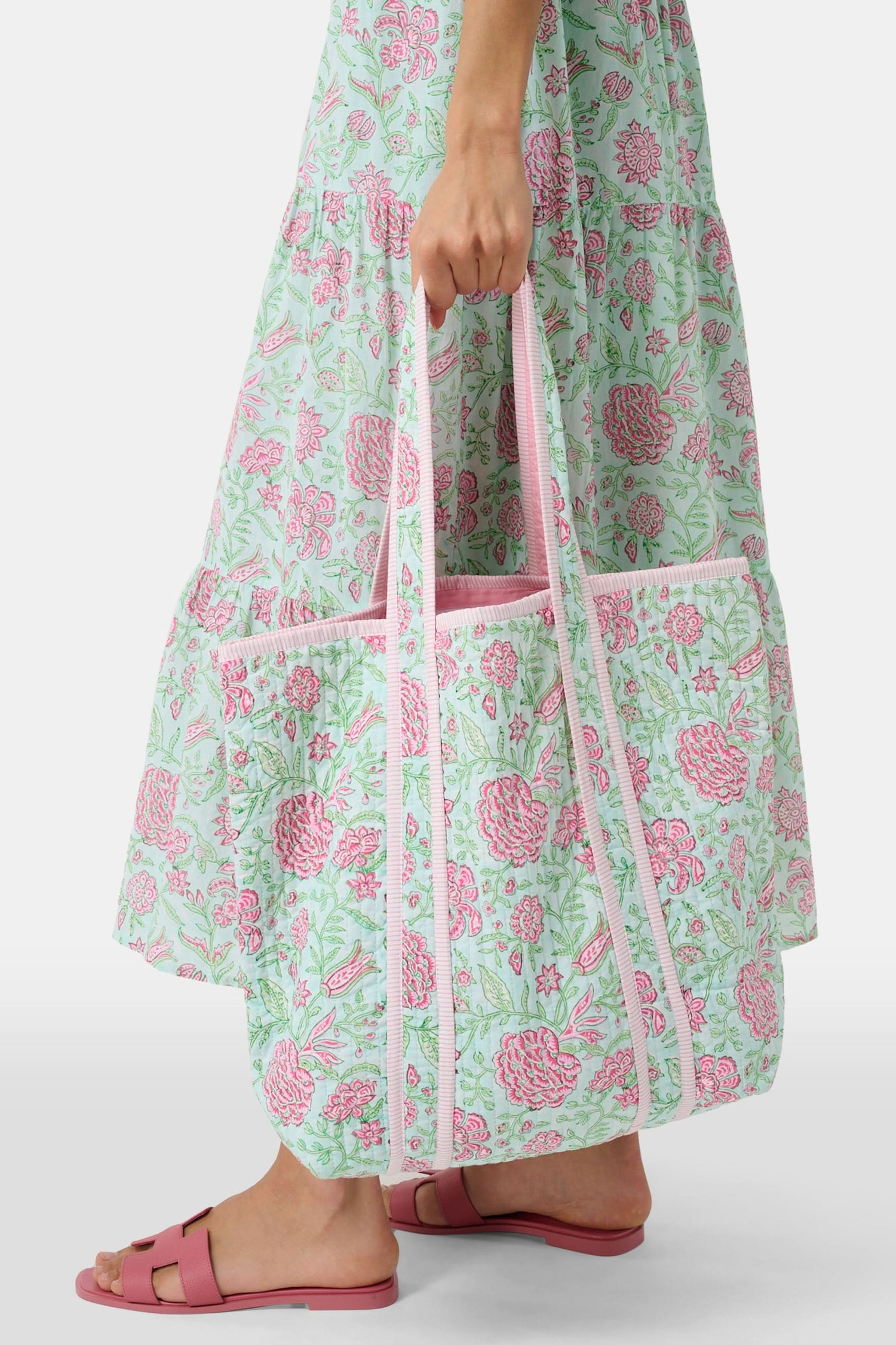 The Roller Rabbit Camellia Block Quilted Tote features pink and green floral patterns, a pale pink interior lining, and long white handles, shown on a plain white background.
