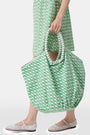 The Cane Bondi Bag by Roller Rabbit is a green and white tote with a wide, round handle, side ties, and a repeating fish pattern on soft cotton canvas. Its unique flared shape adds style to this charming everyday bag.