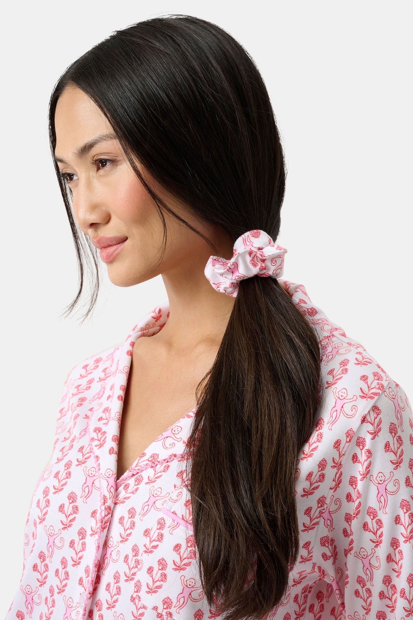 The Rosa Ditsy Monkey Scrunchie by Roller Rabbit features a pink fabric with a red floral print, shown against a white background. This soft scrunchie is gentle on hair.