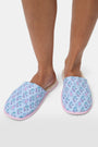 The Rosa Ditsy Monkey Quilted Slippers by Roller Rabbit feature a blue floral pattern, pink striped soles, and faux-shearling lining, displayed side by side on a white background.